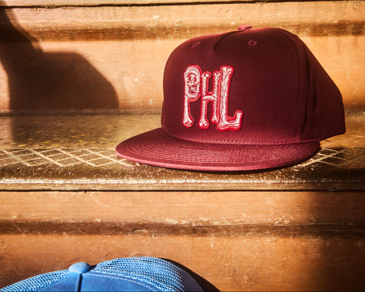 Philadelphia Phillies PHL skull and bones snap back hats in Phillies maroon and Philadelphia Phillies light blue design. Maroon 5 panel snapback, light blue 5 panel surf style hat with corded brim